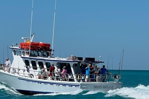 A white boat with people on board travels through the ocean.