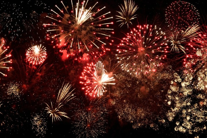 A vibrant display of red, gold, and white fireworks against a dark night sky.
