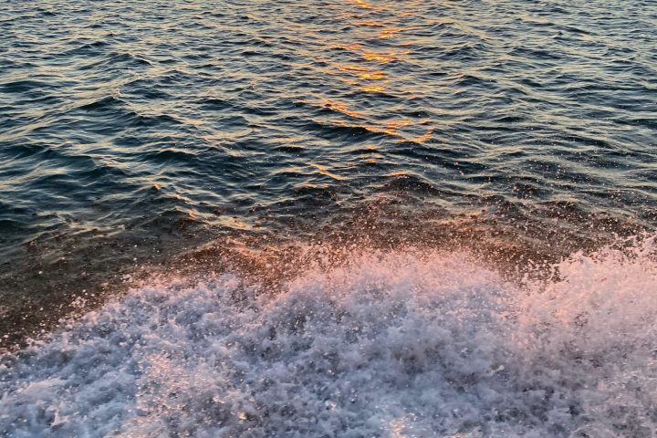 Sunset over ocean with waves crashing on the shore.