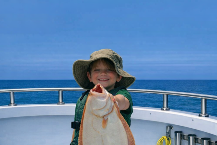 Child on boat holding large flat fish, smiling, wearing a hat.
